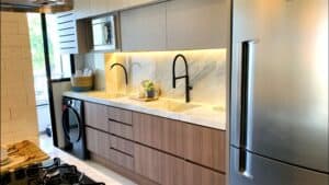 Modern kitchen with wooden cabinets, marbled countertop, black appliances, and a stainless steel refrigerator. Under-cabinet lighting is visible, showcasing the meticulous countertop installation as part of the elegant kitchen remodeling.