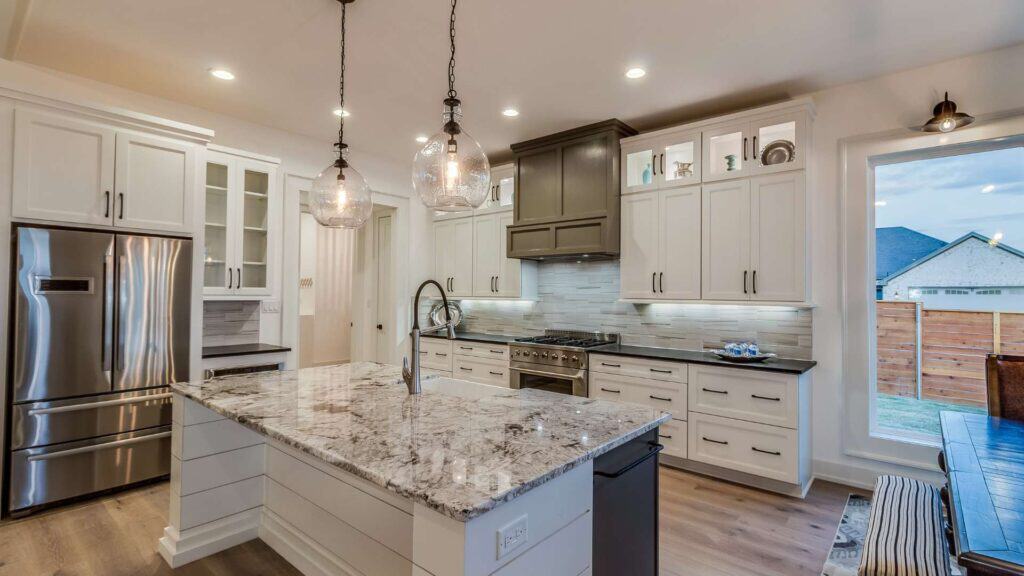 Modern kitchen with white cabinets, stainless steel appliances, marble countertops from expert countertop installation, large island with sink, and pendant lighting.