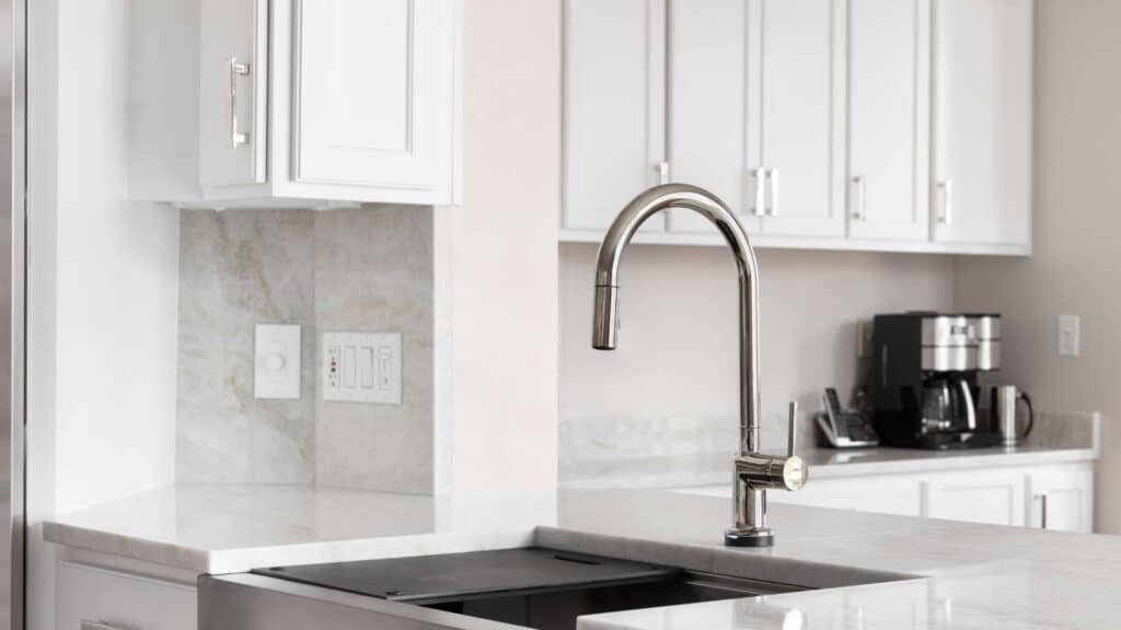 Modern kitchen with white cabinets, a stainless steel faucet over a sink, and a coffee maker on the countertop in the background. The sleek design hints at recent kitchen remodeling, perfectly blending style and functionality.