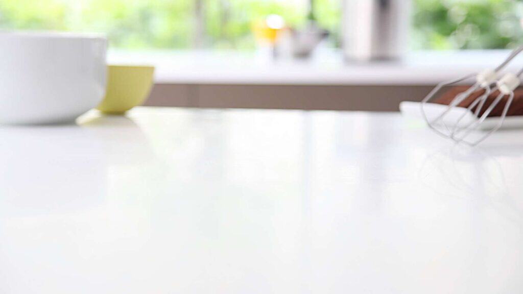 A blurred kitchen counter scene with a white bowl, a yellow cup, and a whisk. The background features a bright, out-of-focus window, giving it the perfect setting for showcasing ideas on kitchen remodeling.