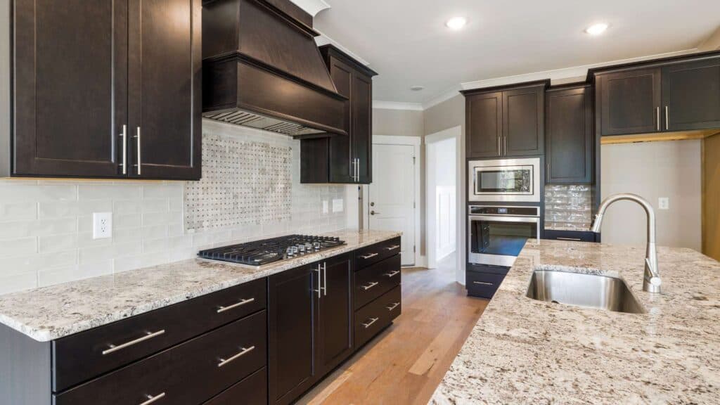 Modern kitchen with dark wood cabinets, granite countertops, stainless steel appliances, a built-in oven and microwave, and a large sink—ideal for any kitchen remodeling project.