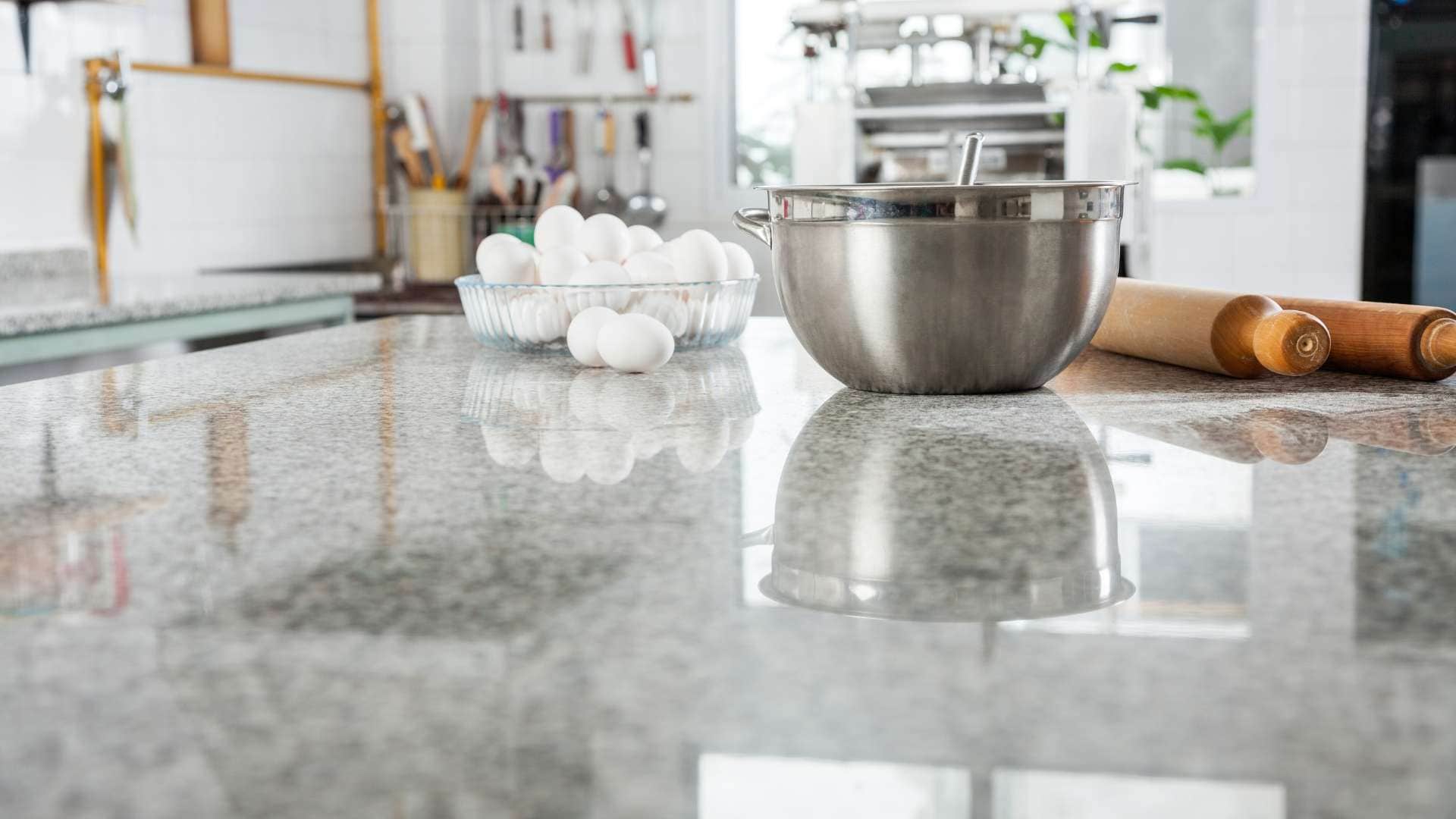 Bowl of eggs, stainless steel mixing bowl, and rolling pin on a granite kitchen counter with cooking utensils in the background, highlighting a recent kitchen remodeling project.