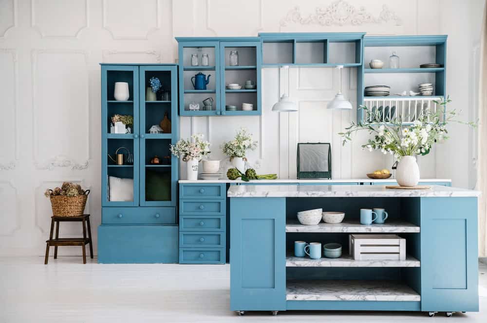 A bright, modern kitchen remodeling in Ocean County, NJ with blue cabinets, marble countertops, open shelving, and pendant lights above a central island. Decor is minimal and elegant.