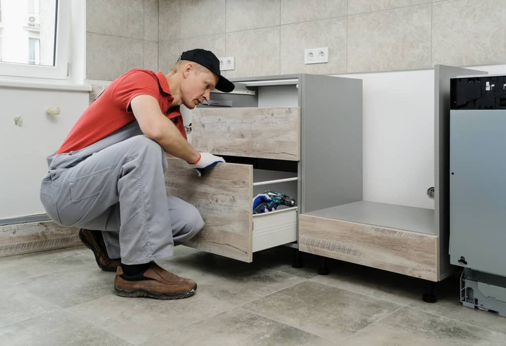 A man in a red shirt and cap installs or repairs drawers in a modern kitchen, showcasing the fine craftsmanship typical of Kitchen Remodeling projects in Ocean County, NJ.